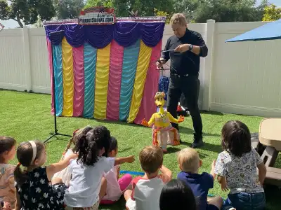 Children enjoying an outdoor guest performance at Newport Ave Preschool summer activities program